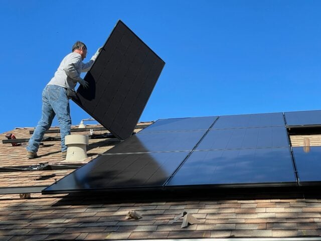 Man holding up a solar PV panel on a roof during an installation.