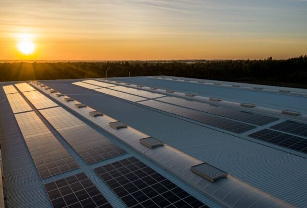 Rows of solar PV panels on a large roof with countryside and sunset in the background.