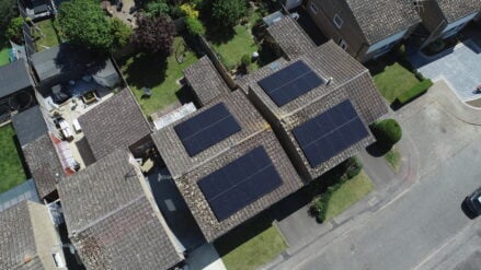 Overhead of four groups of solar PV panels installed across two roofs.
