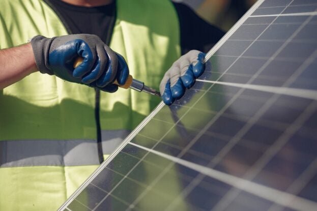 A worker using a screwdriver to install a solar panel.